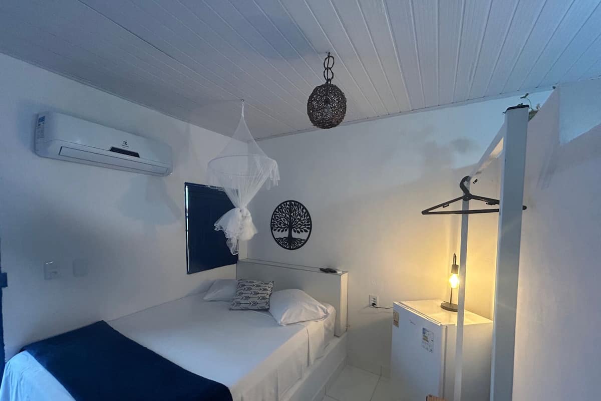 Quarto de hotel com cama, mesa de cabeceira, luminária pendente, ar-condicionado fixado na parede e um enfeite de parede.