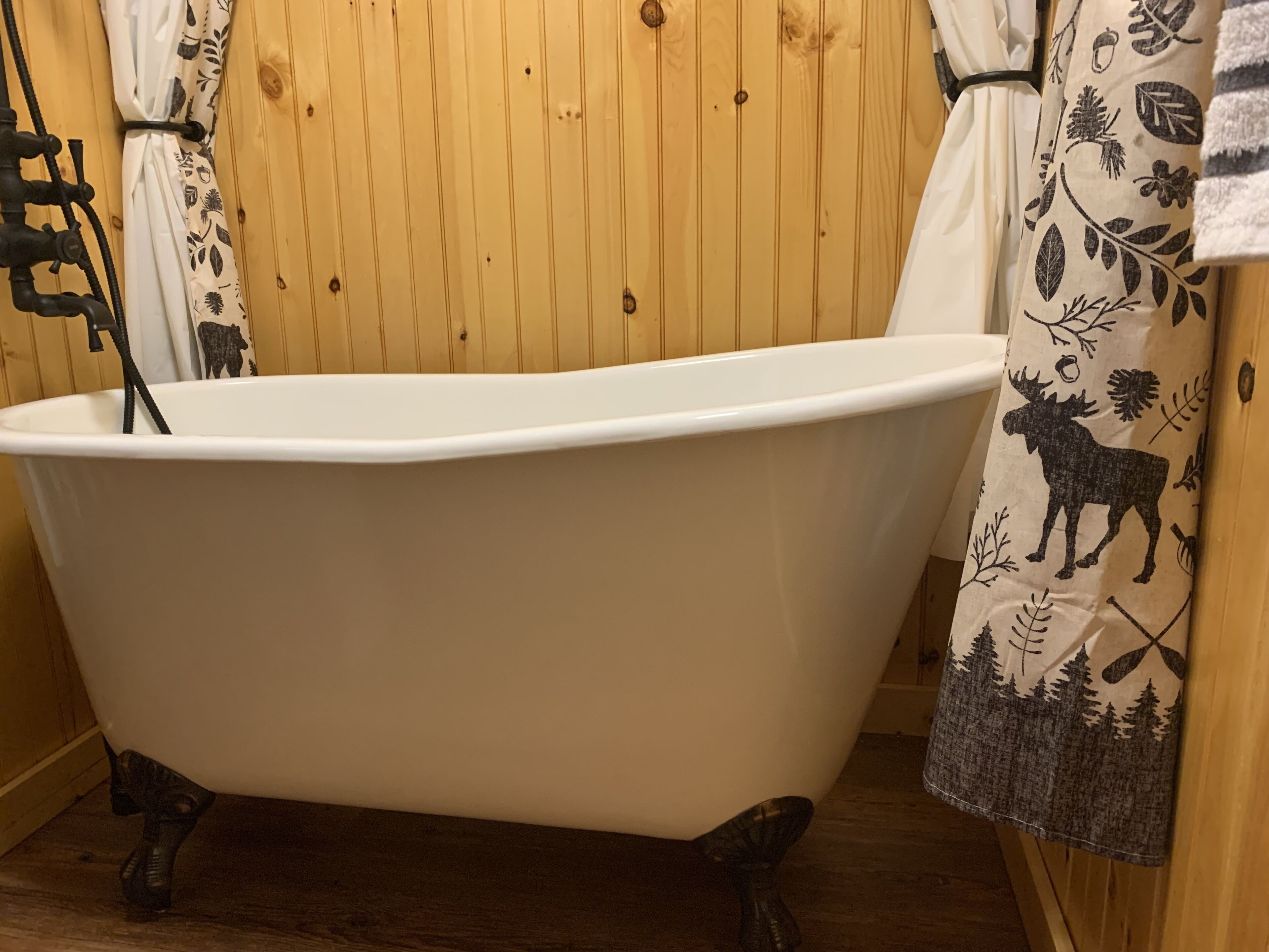Una bañera tipo pata de león en una habitación de madera con un cortinero que muestra un diseño de alce y bosque.