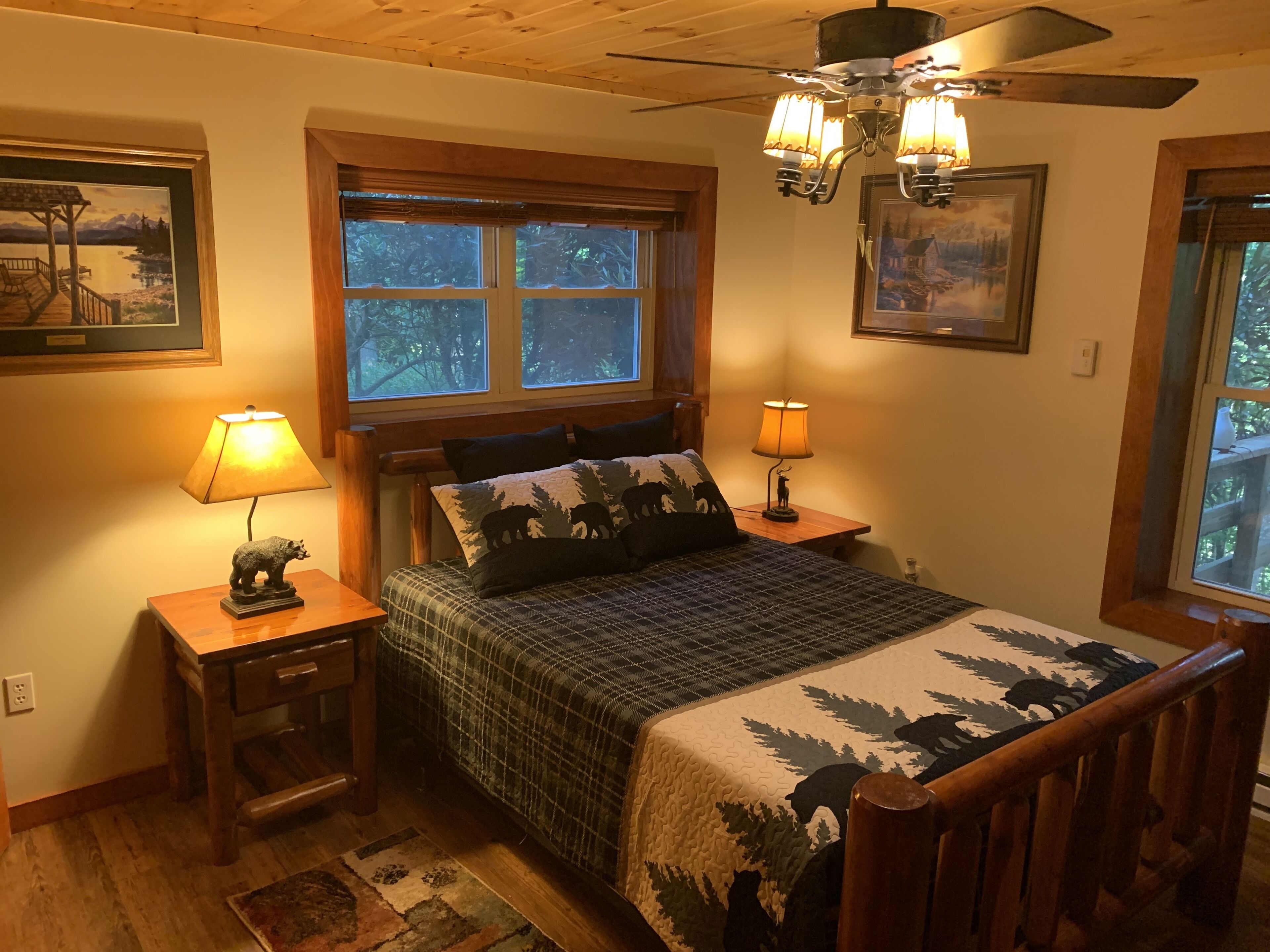 A cozy bedroom with a bed, two bedside lamps, a wooden headboard, a window with blinds, and a ceiling fan.