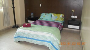 Un dormitorio con una cama, dos mesitas de noche, una lámpara de pie y una ventana con cortinas.