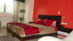 Un dormitorio con cama, mesitas de noche, lámpara y ventana.