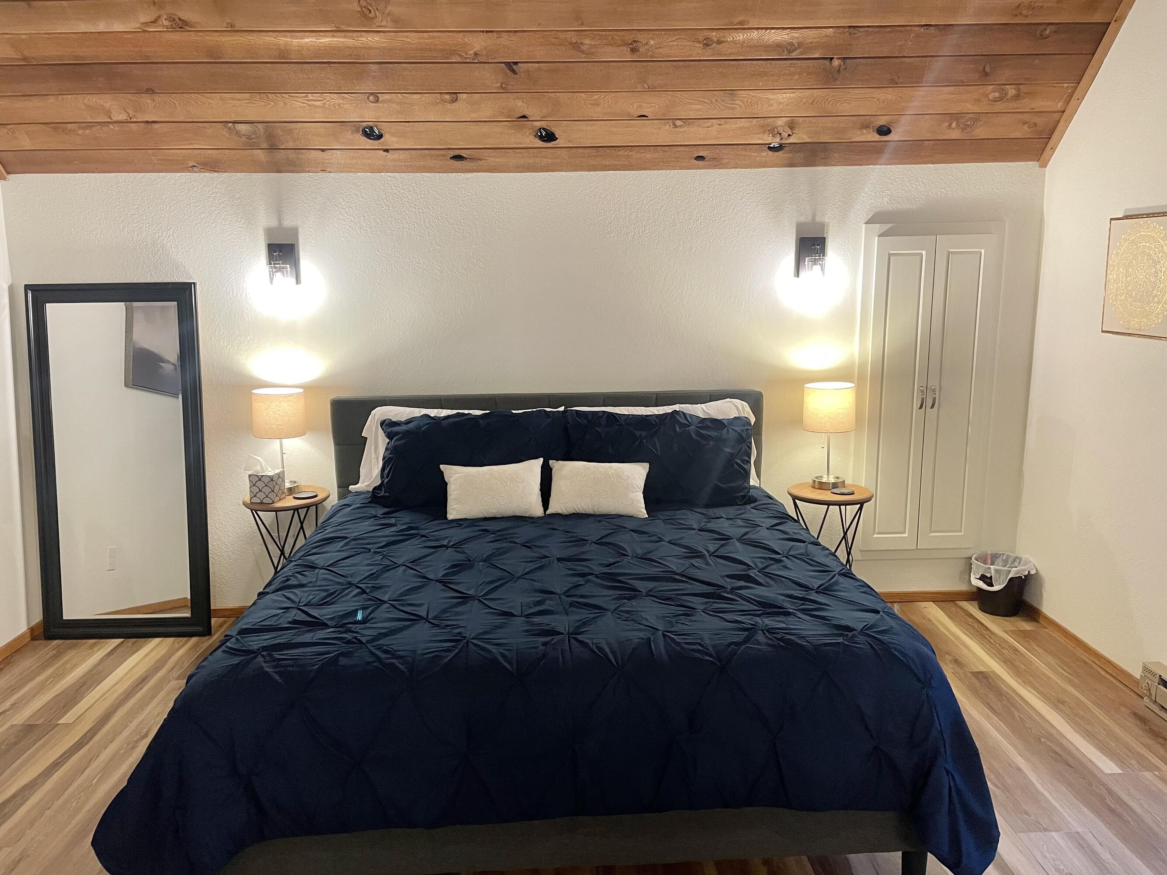 A bedroom with a large bed, two bedside tables, a mirror, and a wardrobe.