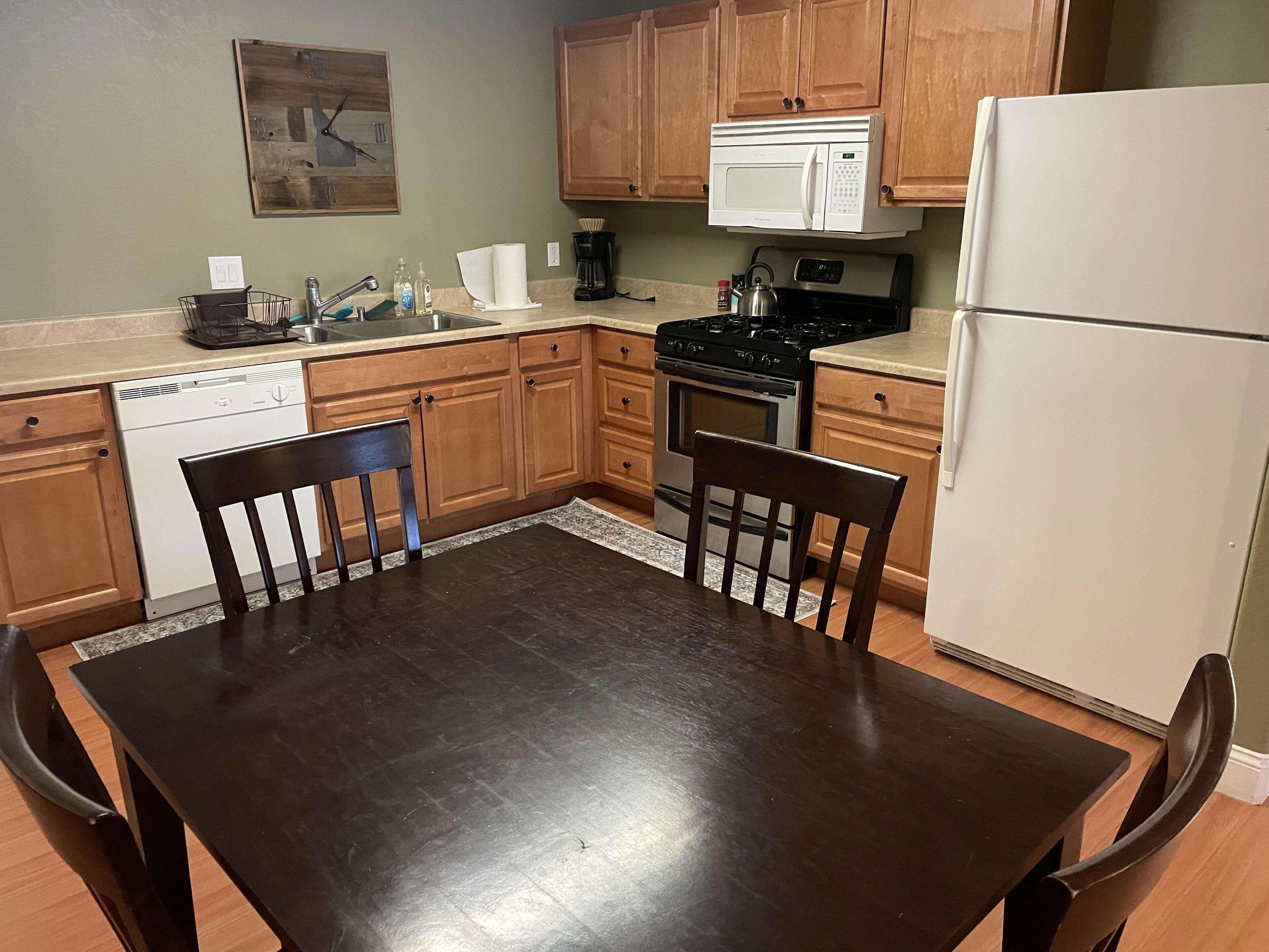 A kitchen with wooden cabinets, a white refrigerator, a stove, and a microwave. There is a dining table with chairs.