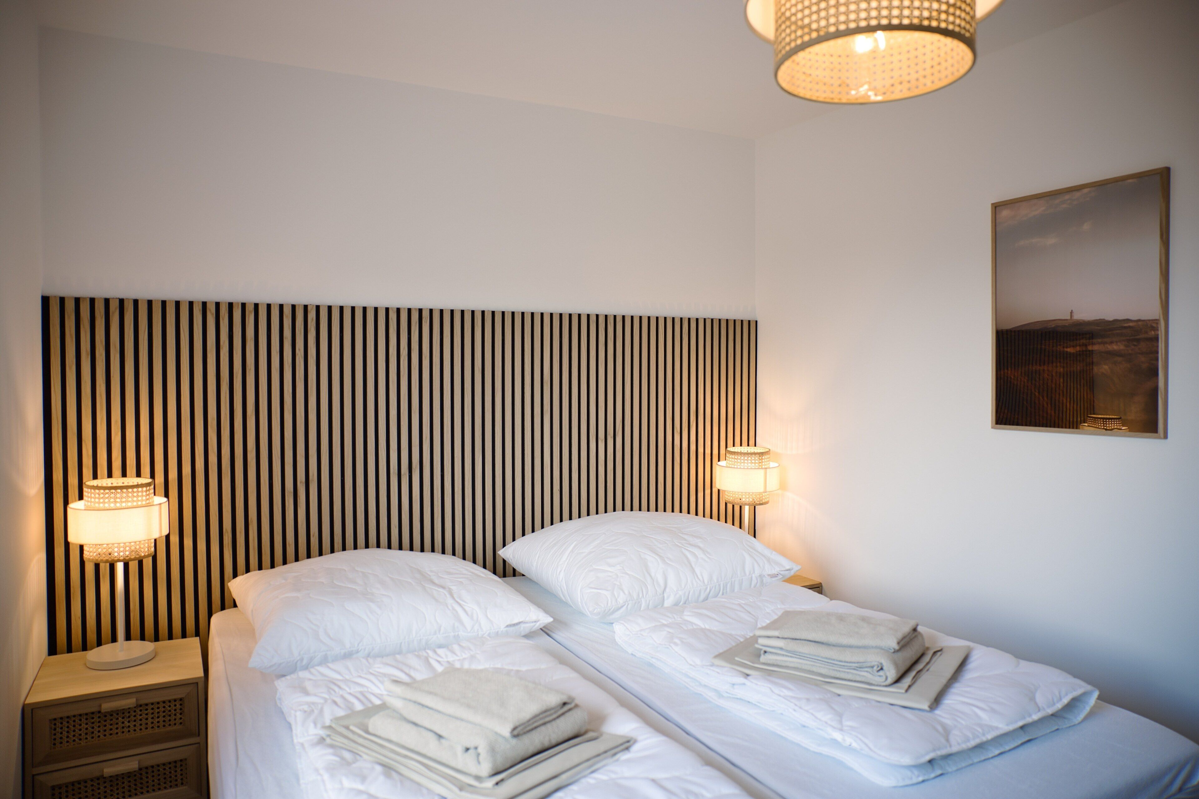A hotel room with a striped headboard, two beds, bedside lamps, and a framed picture on the wall.