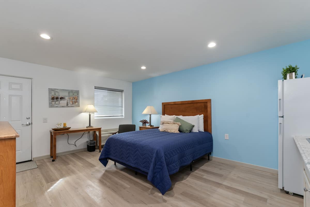 A bedroom with a bed, bedside table, lamp, and a window with blinds.