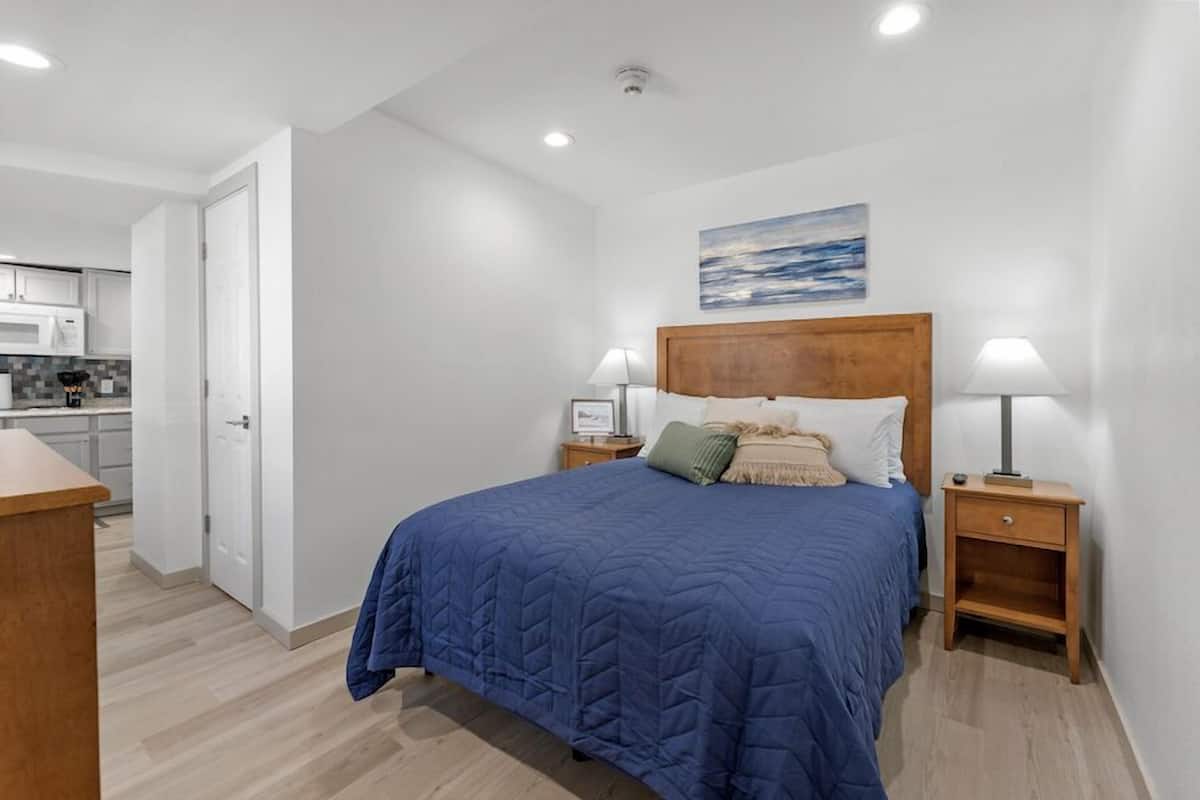 A bedroom with a large bed, two bedside tables with lamps, a wooden headboard, and a painting on the wall.