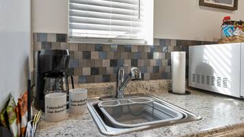 A kitchen with a granite countertop, a stainless steel sink, a coffee maker, and two mugs labeled "Extended Gun Barrel."