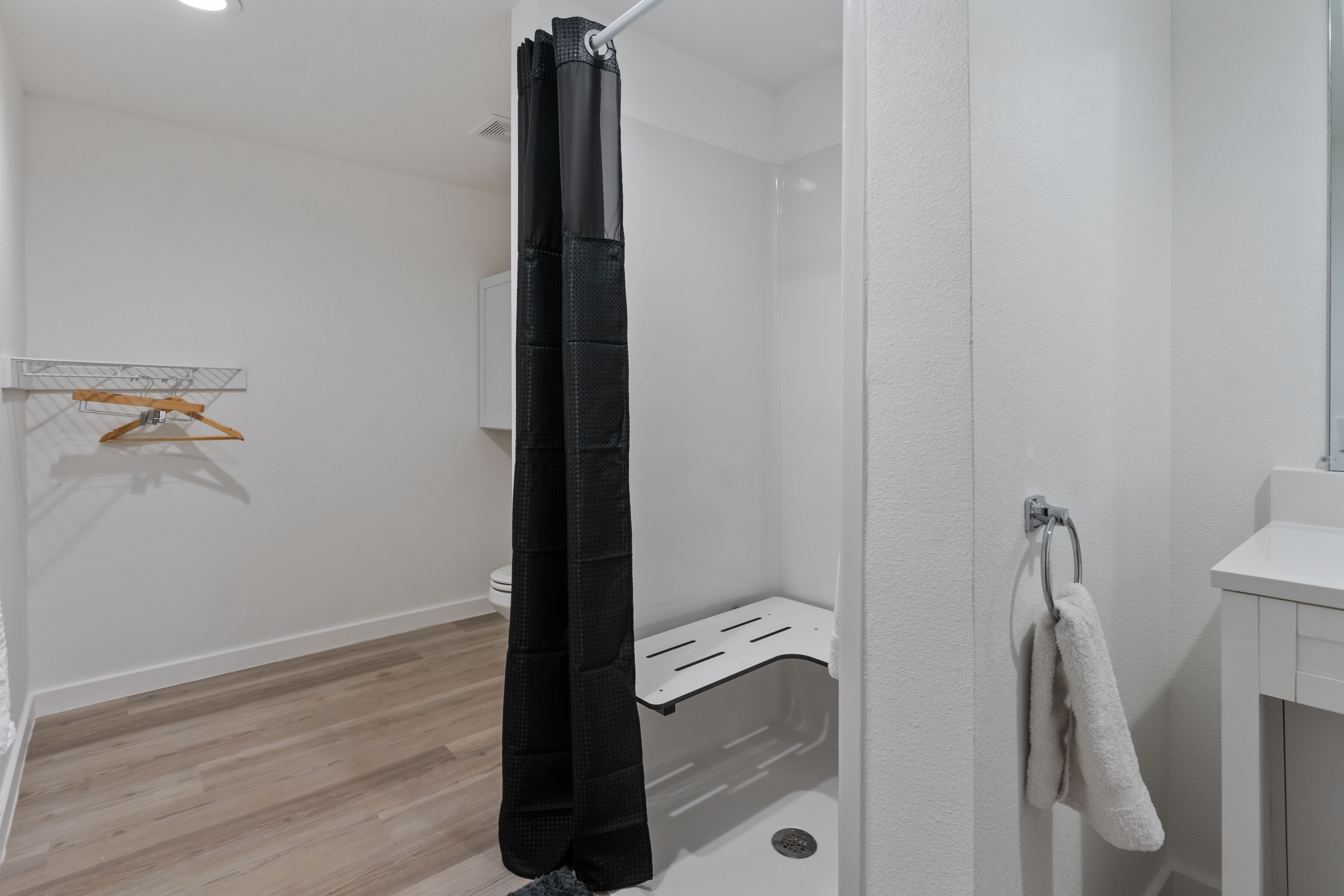 A bathroom with a shower curtain, a towel rack, a white sink, and a wooden floor.