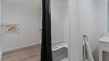A bathroom with a shower curtain, a towel rack, a white sink, and a wooden floor.