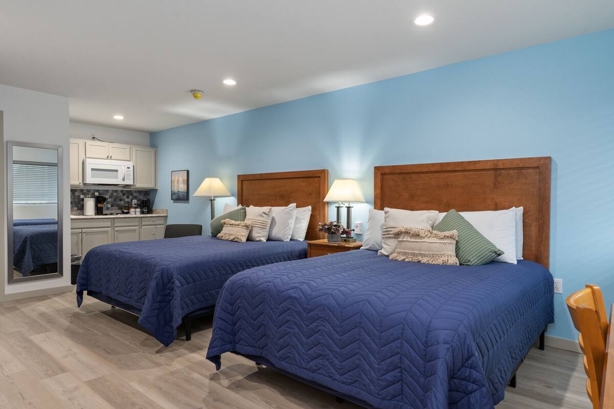 A hotel room with two beds, a kitchenette, and a bathroom.