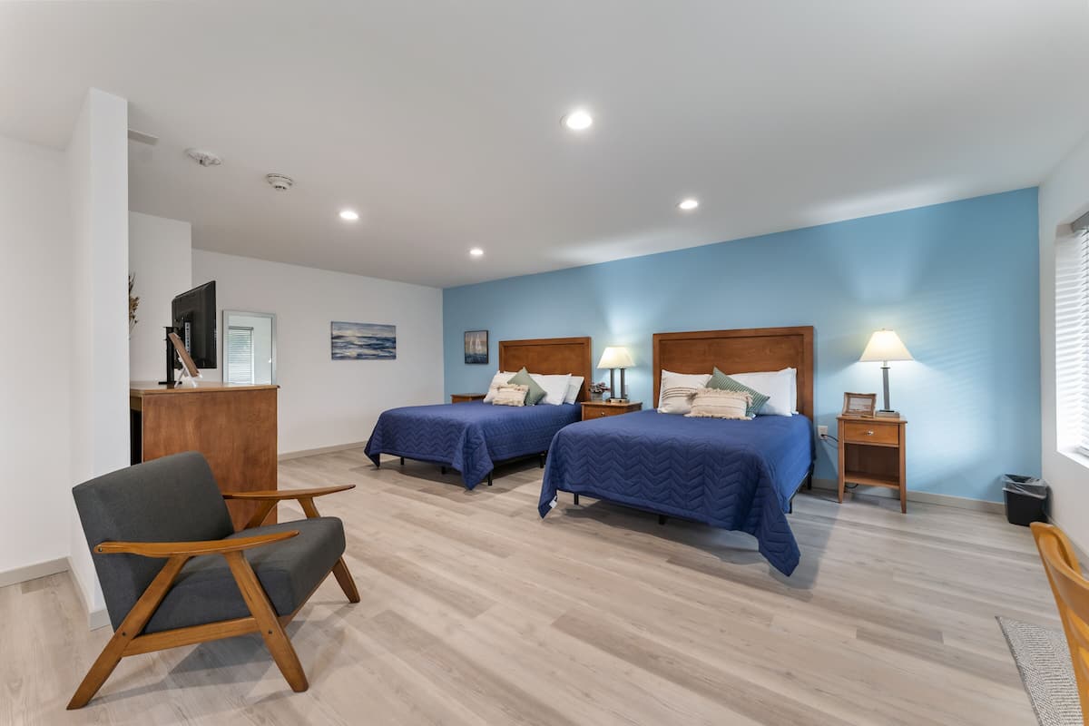 A hotel room with two beds, a desk, a chair, and a TV.