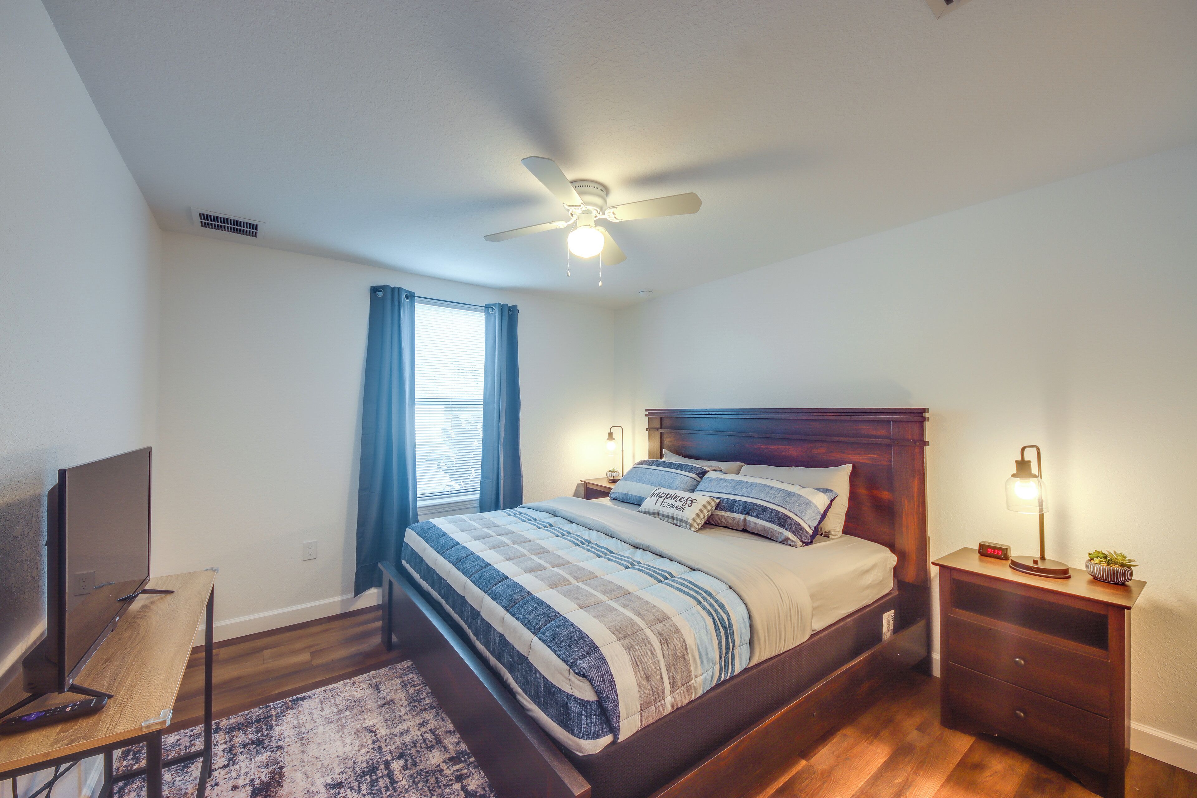 Une chambre à coucher comprenant un lit, un bureau, une télévision, un ventilateur de plafond et une table de chevet avec une lampe.