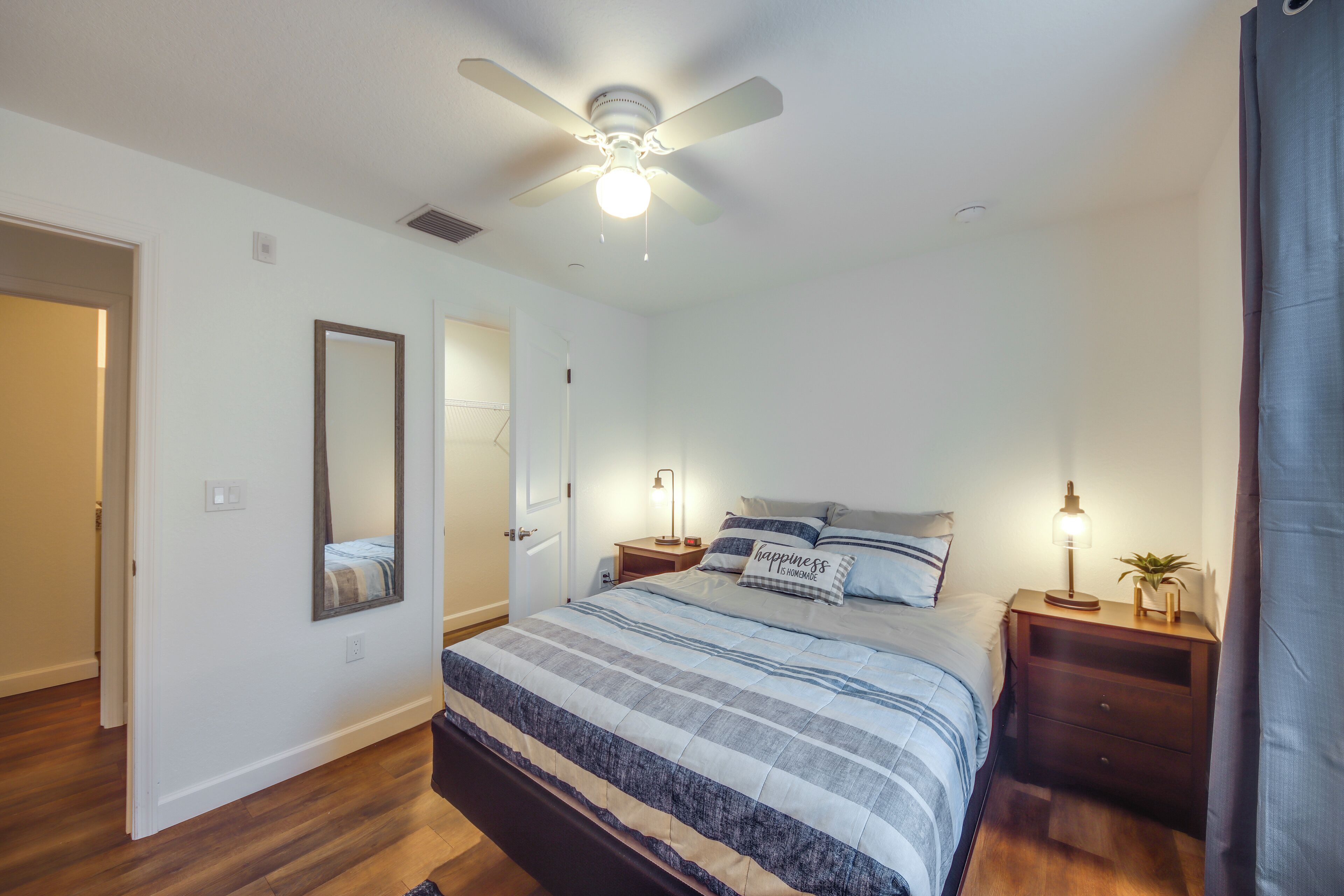 A bedroom with a bed, a nightstand, a mirror, a ceiling fan, and a door.