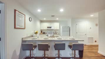 A modern kitchen with white cabinets, a granite countertop, and four bar stools.