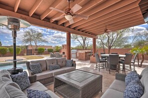 An outdoor patio with a pool, a covered seating area with a table and chairs, and a ceiling fan.