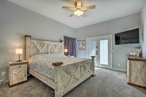 A bedroom with a bed, nightstand, dresser, ceiling fan, and artwork on the wall.