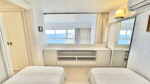Een slaapkamer met twee bedden, een groot raam met uitzicht op de zee, een ingebouwde televisie en een airconditioning.