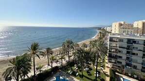 Hotel aan het strand met zwembad, palmbomen en uitzicht op de oceaan.