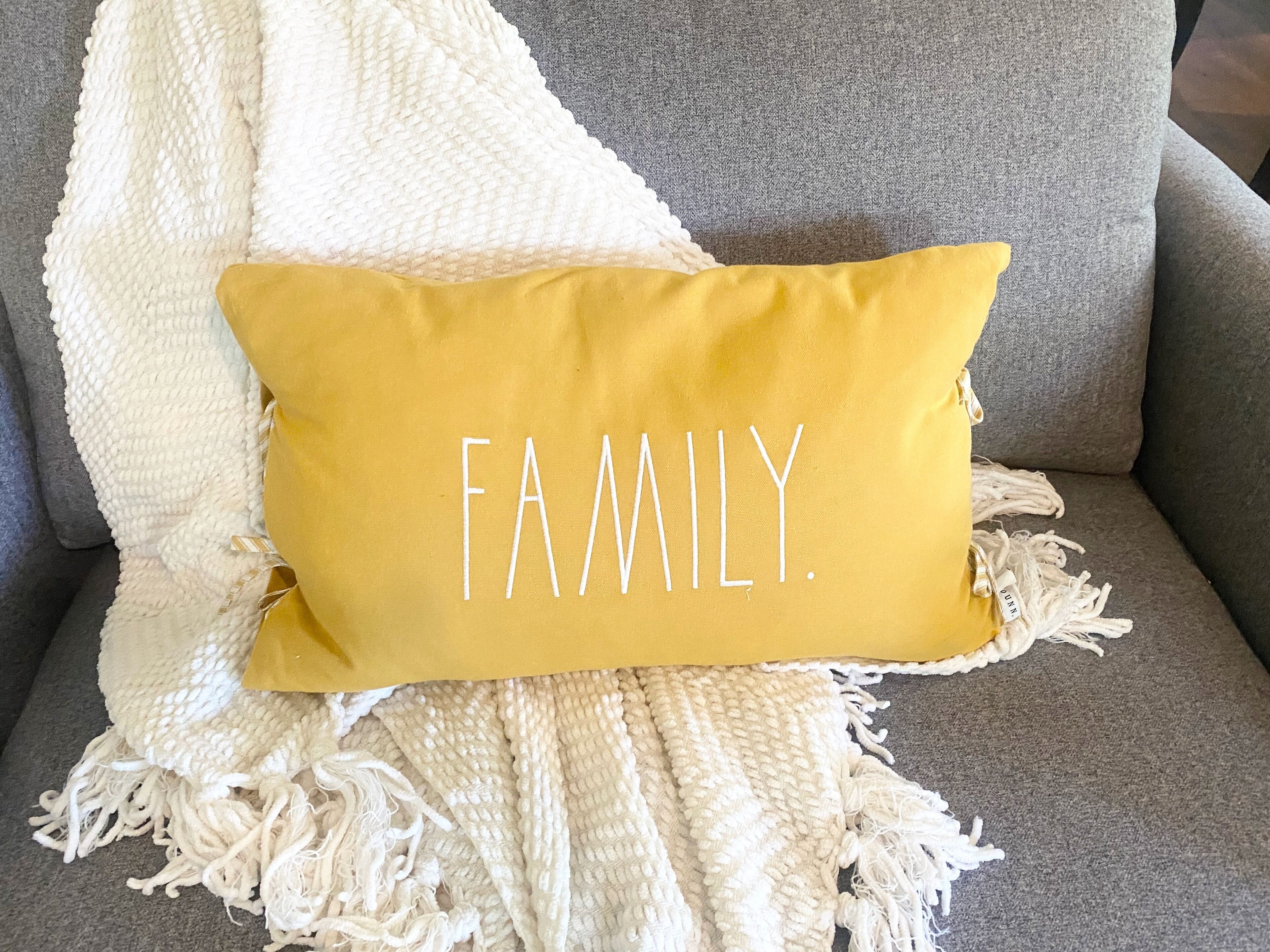 Un sofá con un cojín color mostaza que dice 'FAMILIA'.