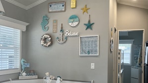 Uma cozinha com bancada de mármore, uma mesa de jantar com um banco e várias decorações de parede, incluindo um cavalo-marinho, uma estrela e um relógio.