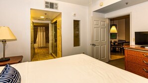 Ein Hotelzimmer mit Bett, Schreibtisch, Lampe, Fernseher, Kommode und einem durch eine offene Tür einsehbarer Badezimmer.