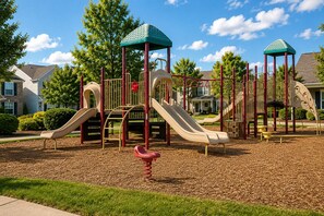 Un parque infantil con toboganes y estructuras para escalar, rodeado de césped y árboles.