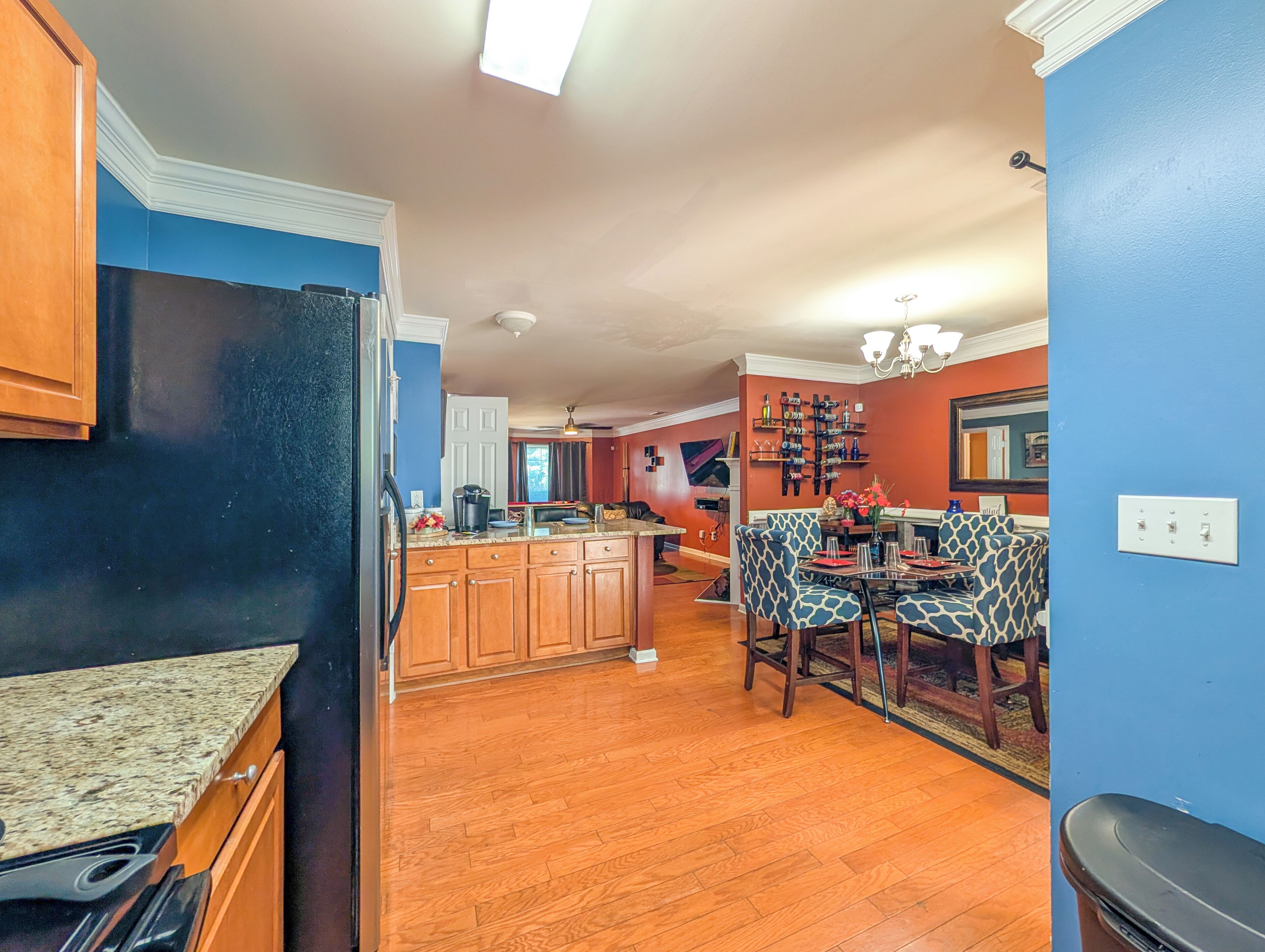 A kitchen with wooden cabinets, a granite countertop, and a dining area with patterned chairs.
