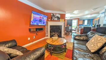 A living room with a fireplace, leather sofas, a television mounted on the wall, and a kitchen in the background.