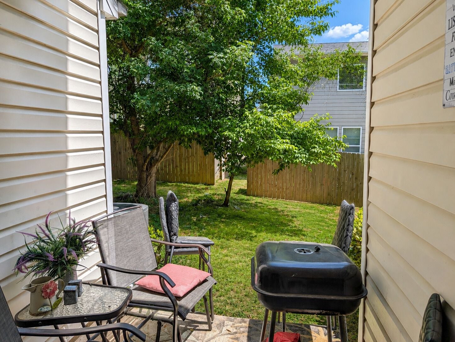 A patio with a grill, chairs, and a small table with a pitcher and plant.