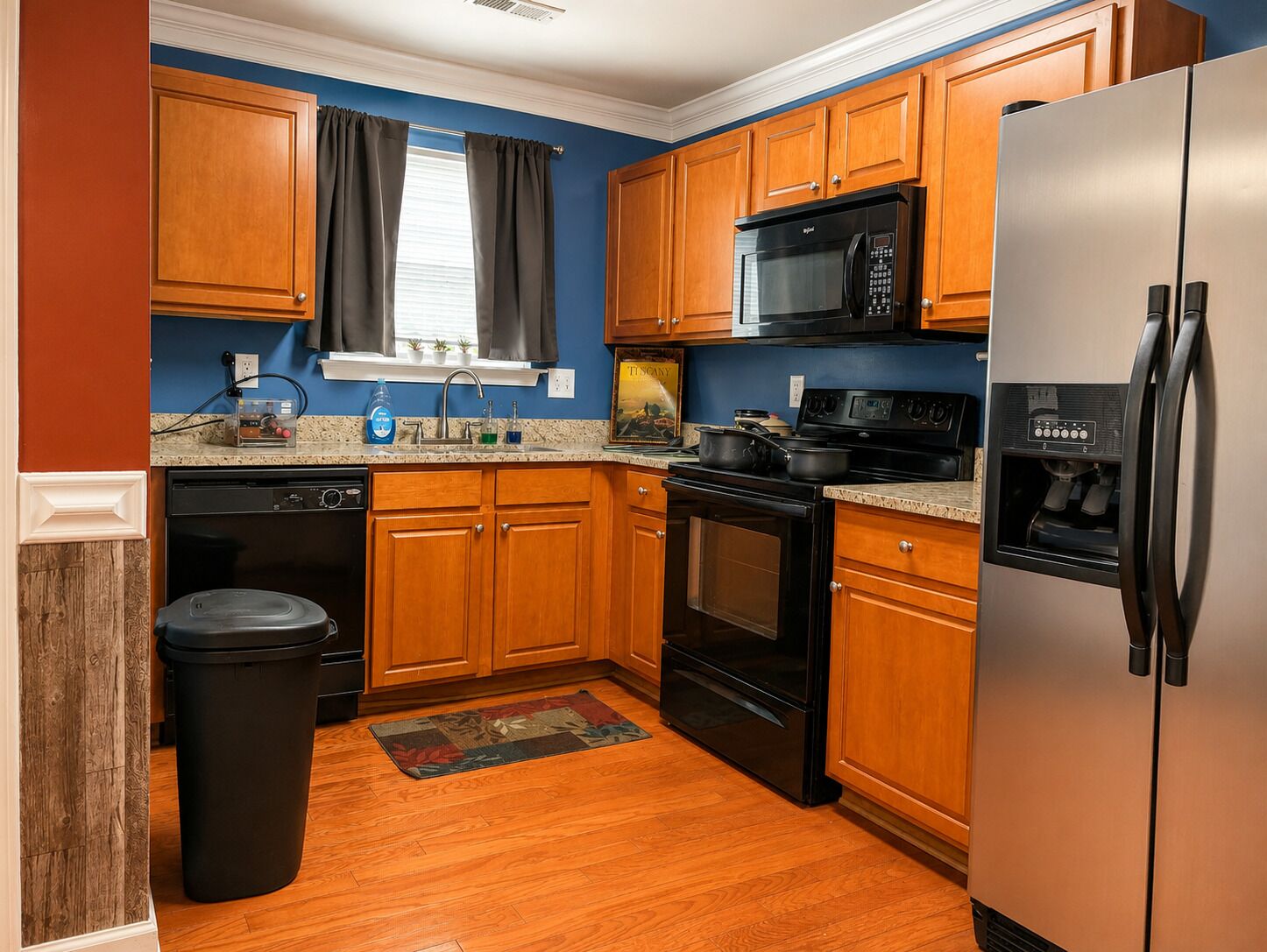 A kitchen with wooden cabinets, a stainless steel refrigerator, a microwave, and a stove.