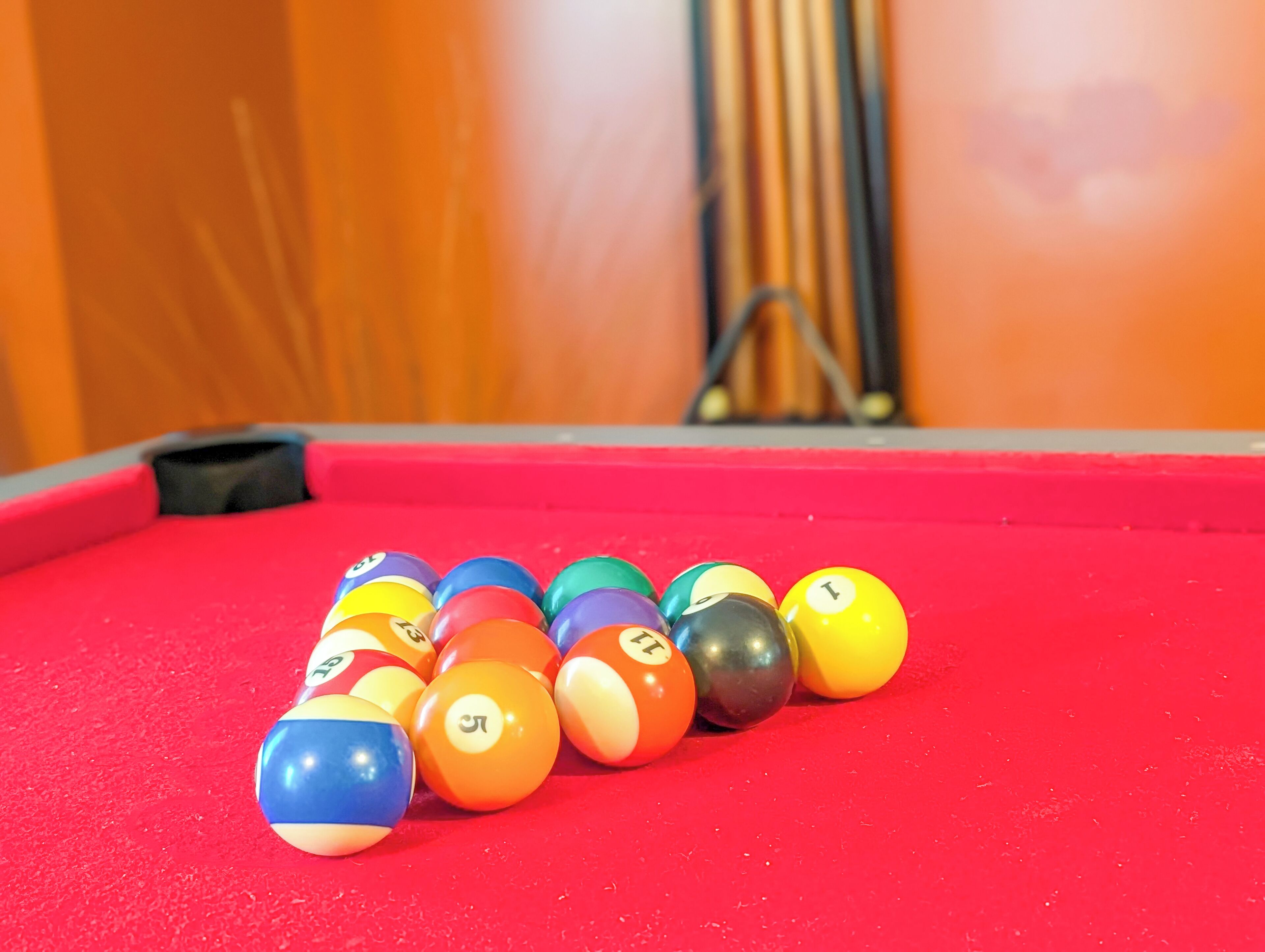 A pool table with a red felt surface and a set of numbered billiard balls arranged in a triangle.