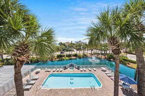 A swimming pool with lounge chairs, palm trees, and a view of a body of water.