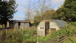 A rustic wooden structure with a sloped roof, surrounded by a wire fence and dense vegetation. - Comfortable house (10 persons), 1,5 km from the sea (Finistère Sud - Bretagne) (Plozévet)