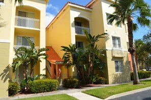 A yellow building with balconies and palm trees. -  Resort Style Vacation Condo with keyless entry (Palm Beach Gardens)