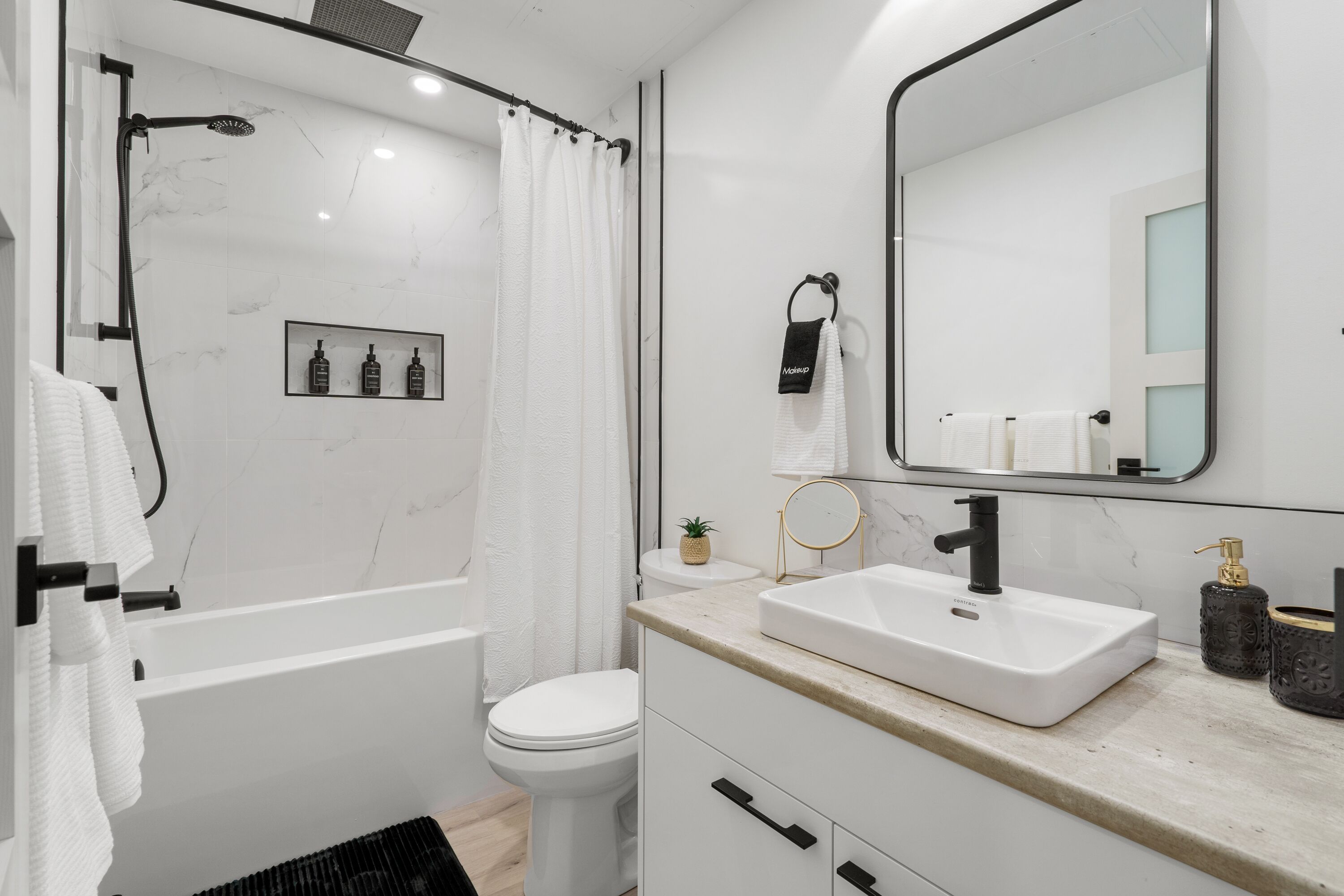 Un baño moderno con bañera, inodoro y tocador con lavamanos y espejo.