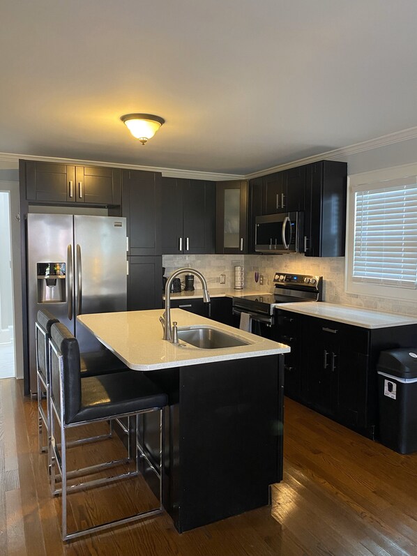 A modern kitchen with dark cabinetry, stainless steel appliances, a bar area, and a window with blinds.