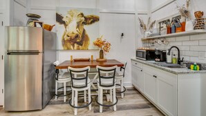 A modern kitchen with a stainless steel refrigerator, a wooden dining table with four chairs, and a large painting of a cow on the wall. - Romantic Couples Cottage, Large Covered Deck with Hot Tub, TV,  Couches, Firepit (Clarkesville)