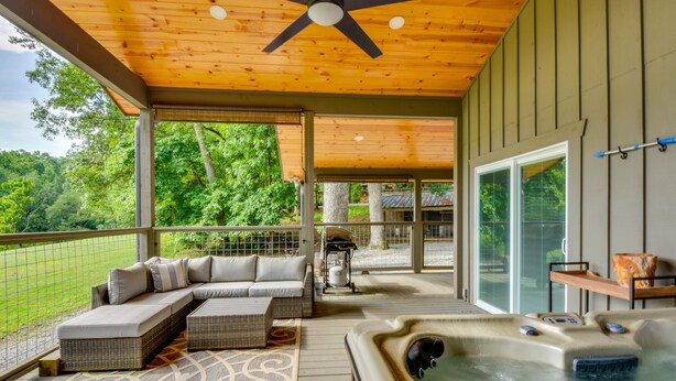 A covered outdoor deck with a hot tub, seating area, and a view of the surrounding greenery. - Romantic Couples Cottage, Large Covered Deck with Hot Tub, TV,  Couches, Firepit (Clarkesville)