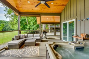A covered outdoor area with a hot tub, seating, and a view of the surrounding greenery. - Romantic Couples Cottage, Large Covered Deck with Hot Tub, TV,  Couches, Firepit (Clarkesville)