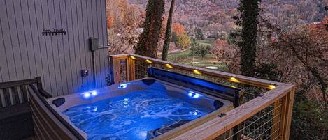 Un bain à remous avec une terrasse en bois et une vue sur une vallée boisée.