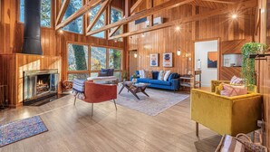 Amplia sala de estar con chimenea, vigas de madera, ventanas grandes y un rincón de descanso acogedor.