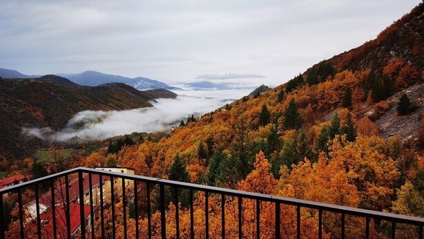 Paisaje montañoso con follaje otoñal, un valle y una vista distante de montañas.