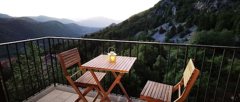 A balcony with a wooden table and two chairs, overlooking a mountainous landscape.
