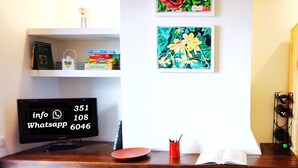 Una habitación con un escritorio, una computadora y dos cuadros enmarcados con motivos florales en la pared.