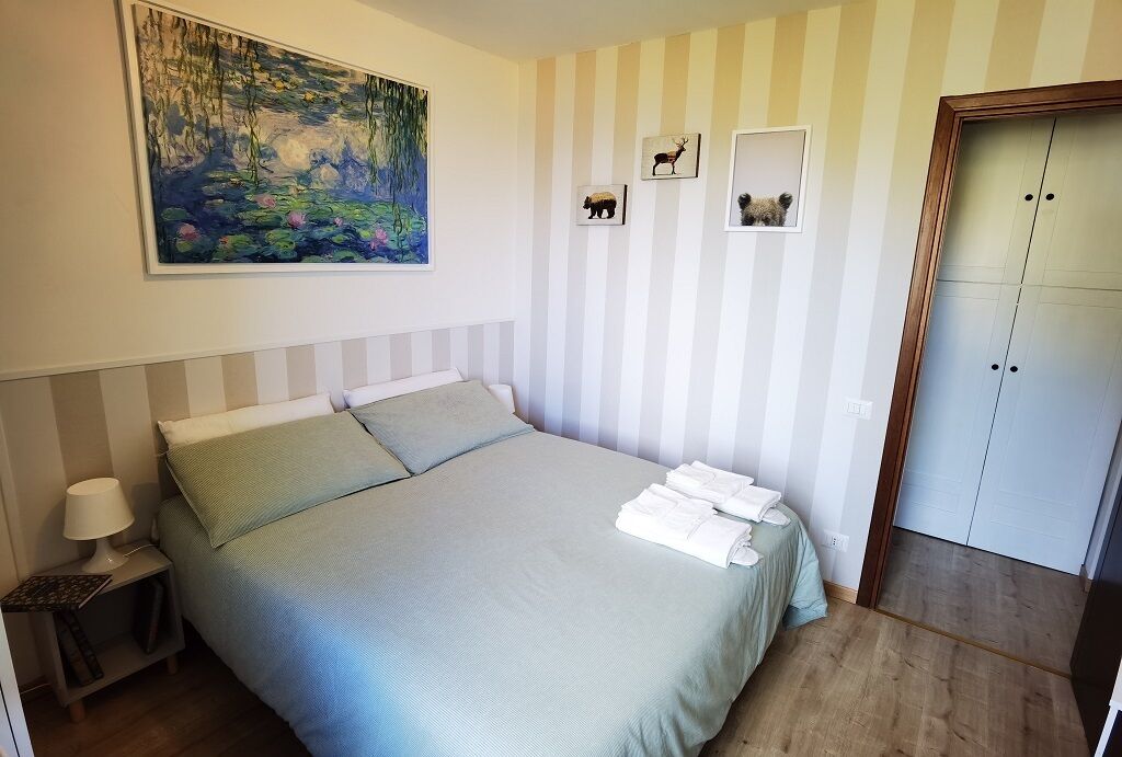 Een slaapkamer met een bed, nachtkastje, schilderij en een garderobe.
