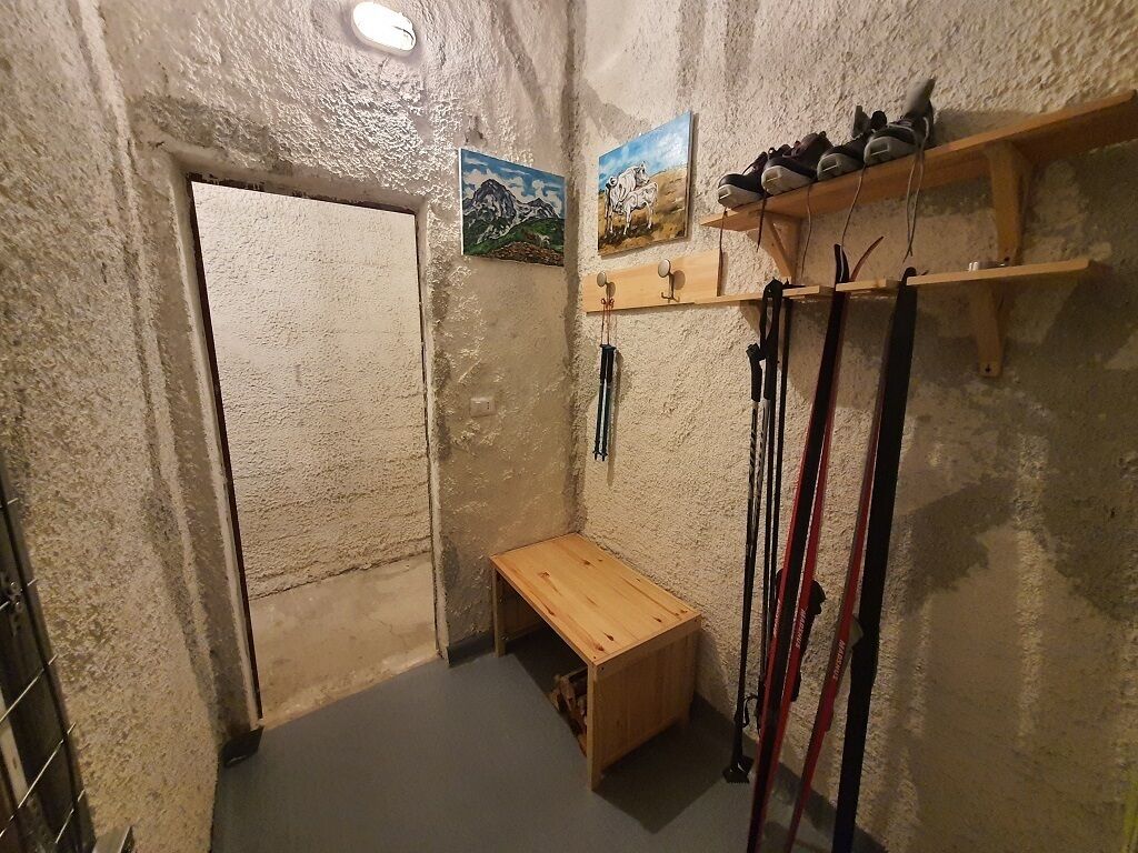 A small room with a wooden bench, a door, and a shelf with shoes and ski poles.
