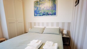 Una cama bien hecha con toallas dobladas, un cuadro de nenúfares en la pared y un armario cerrado.