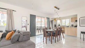 Un salon moderne avec un canapé gris, une table à manger avec des chaises et un coin cuisine doté de meubles en bois et d’un dosseret carrelé.