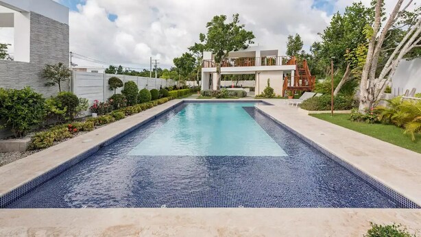 Une piscine rectangulaire bordée de carreaux, entourée d’un jardin aménagé avec différentes plantes et arbres.
