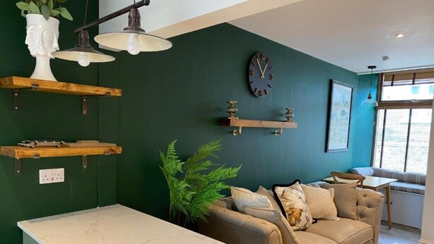 Una cocina moderna con encimera de mármol, pared verde, sofá y comedor con vistas al exterior.